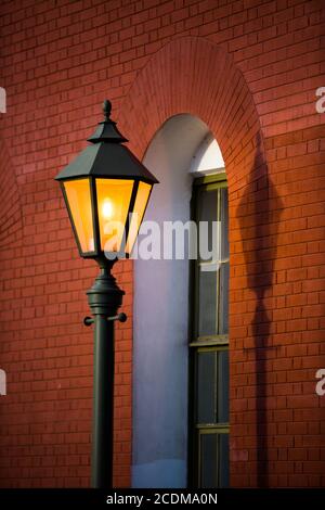 Orange light from a street lamp. Glowing historic street lamp, red brick wall on background, vertical. Lantern at night Stock Photo