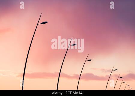 Silhouette of curved street lights during dramatic sunset sky Stock Photo