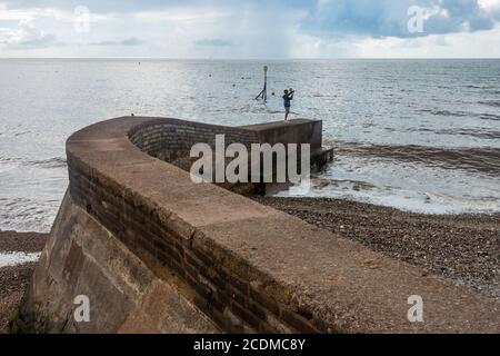 A man stands alone at the end of a curving stone wall which juts out into the sea at Sidmouth in South Devon, UK Stock Photo