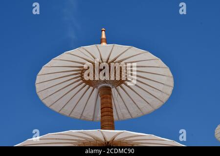 Upward persepctive view of a white paper parasol against a bright blue sky background. Stock Photo