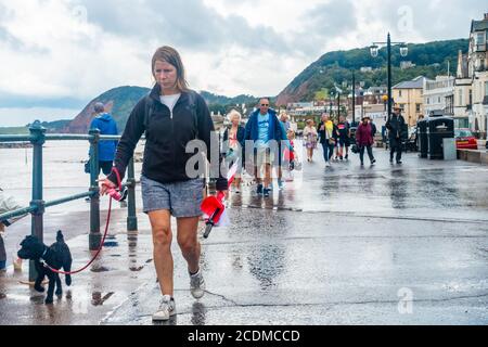 People walk up and down the esplanade at Sidmouth beach in Devon, UK despite it being wet and rainy weather. Stock Photo