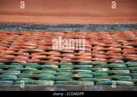 Shallow perspective view of green and red terracotta roof tiles on a buddhist temple in Asia. Stock Photo