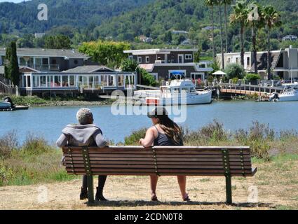 two  woman friends, one black one white,  talk on a bench during the covid 19 restrictions in larkspur california Stock Photo