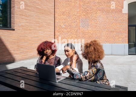 multiracial girls students sitting outdoor the university using a laptop computer - three schoolgirls connected on line in a school campus Stock Photo