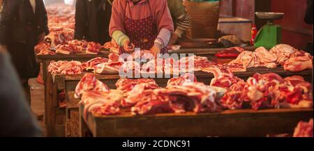 Vietnamese female butcher cutting fresh pork meat at butchery counter in wet market in Sa Pa, Vietnam. Focus on pork meat. Stock Photo