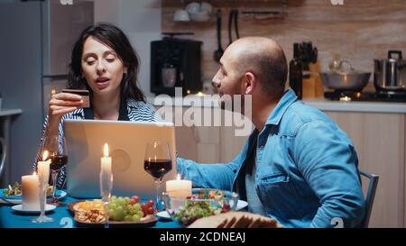 Modern happy couple shopping online on laptop during romantic dinner. Adults sitting at the table, searching, browsing, surfing, using technology card payment, internet Stock Photo