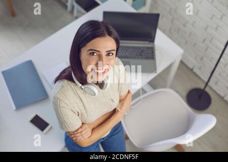 Cheerful remote employee in headphones standing near laptop and smartphone Stock Photo