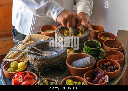 Chef preparing a traditional Pasilla Chili Sauce with all the ingredients, Oaxaca, Mexico. Focus on mortar, blur motion. Stock Photo