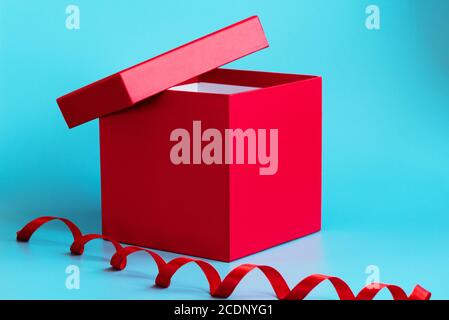Red gift box with lid ajar and spiral ribbon on blue background. Closeup. Holidays concept. Mockup for greeting or advertising Stock Photo