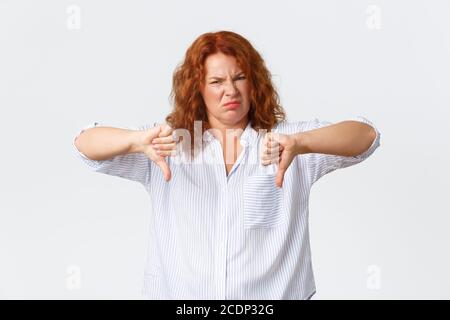 Disgusted middle-aged redhead woman, female entrepreneur grimacing dissatisfied, pointing fingers down and shaking head in rejection, dislike and Stock Photo