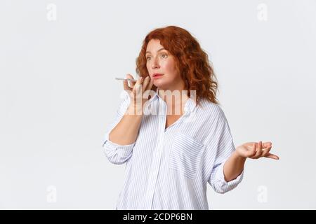 Technology and communcation concept. Portrait of confused middle-aged redhead woman record voice message. Caucasian female talking into smartphone Stock Photo