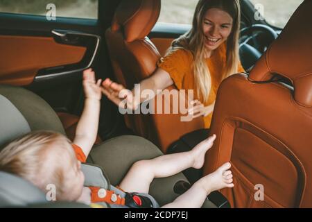 Mother with child in car on road trip high five hands baby sitting in safety seat woman driver family vacation travel lifestyle happy emotions Stock Photo