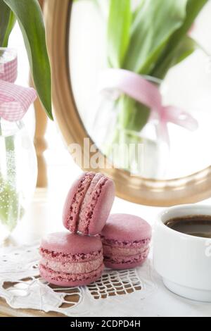 Three pink macaroons and cup of coffee, pink tulips and mirror, backlight background Stock Photo