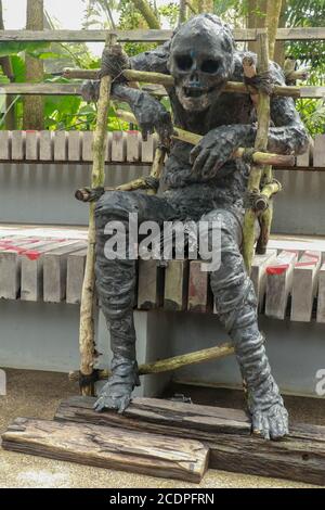 Mummy covered by clothes in skull decorated at halloween cosplay and light on dark background. A figure of a black mummy sitting on a bench. Zombie in Stock Photo