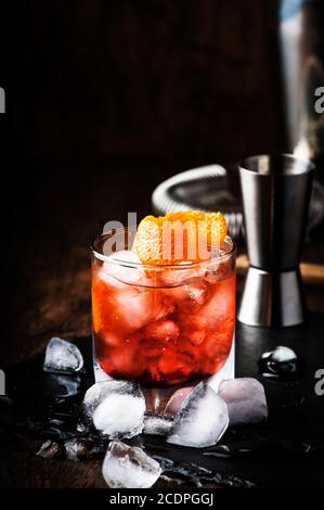 Americano Alcohol cocktail with red vermouth, bitter, soda, orange zest and ice, dark wooden bar counter background, bar tools, selective focus Stock Photo