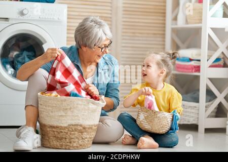 Happy grandma and child girl little helper are having fun and smiling while doing laundry at home. Stock Photo