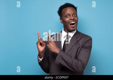 Funny young african american man in suit pointing index fingers aside up. Stock Photo