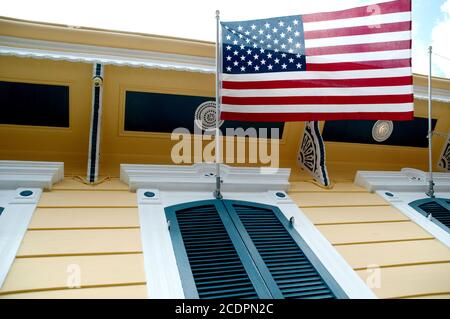 An American flag, the stars and stripes, hanging over the shuttered window of a yellow shotgun house, French Quarter, New Orleans, Louisiana, USA. Stock Photo
