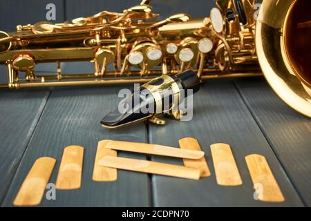 saxophone mouthpiece with metal clamp and gold adjustment hardware, with replacement reeds and instrument body on gray wooden background Stock Photo