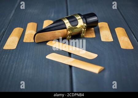 Replacement reeds and saxophone mouthpiece with clamp and golden adjustment screws on gray wooden table Stock Photo