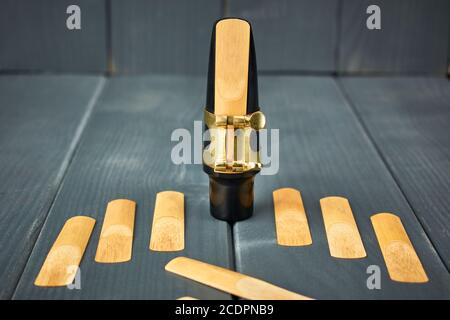 saxophone mouthpiece and reed with clamp and gold hardware along with replacement reeds on gray wooden background Stock Photo