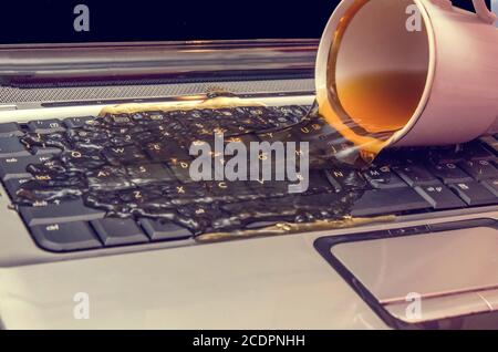 Coffee is poured from a Cup on the laptop Stock Photo