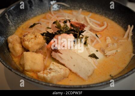 A bowl of laksa, typical soup from southeast asian which consists in wheat noodles, chicken, prawns and fish, served in spicy curry coconut milk Stock Photo