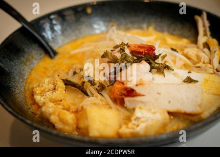 A bowl of laksa, typical soup from southeast asian which consists in wheat noodles, chicken, prawns and fish, served in spicy curry coconut milk Stock Photo