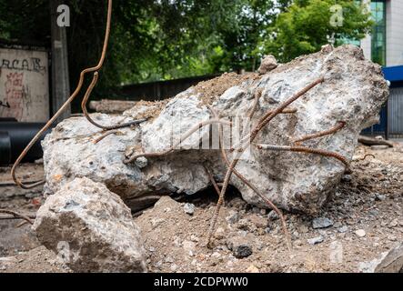 Armature sticks out from concrete block. Ruined construction lying on city road nead green trees in summer day. Huge fragment on building, destroyed p Stock Photo