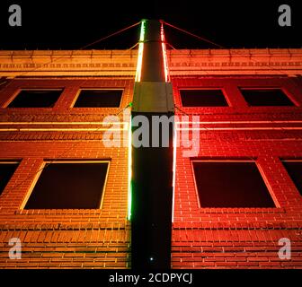 A brick building with dark windows is lighted at night with bright red and green neon lights Stock Photo