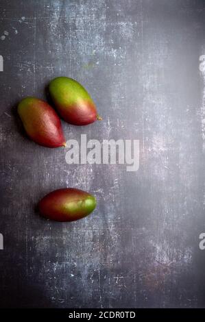 set of mangoes, cut and uncut, on a black, dark, metallic, cement, marble, stone background. Stock Photo