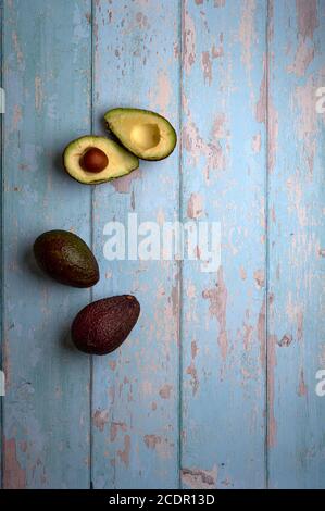 set of avocados, cut and uncut, on a light blue background of deteriorated wood Stock Photo