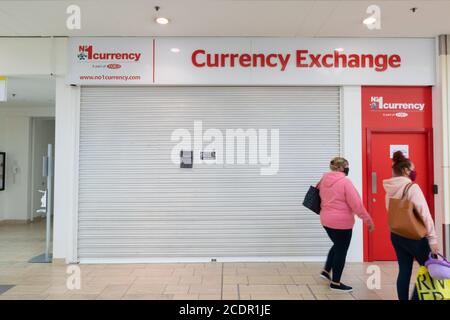 Women with face masks walk pass a closed currency exchange store