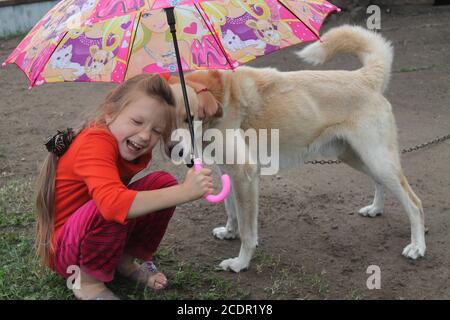 girl under bright umbrella play under rain  in the garden in last summer day on vacation Stock Photo