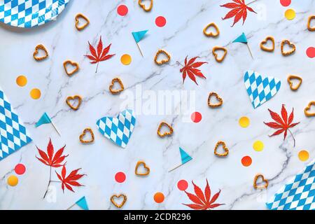 Oktoberfest party background with seasonal decorations, red and yellow confetti and maple leaves. Flat lay on marble table. Bavarian blue white checke Stock Photo