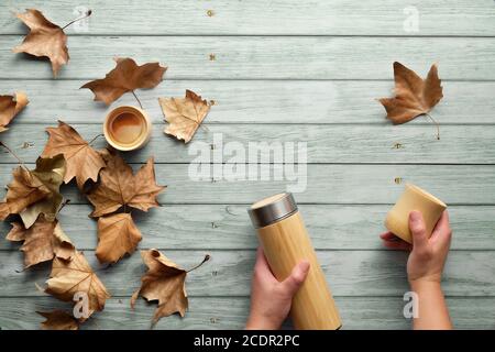 Zero waste eco friendly insulated metal flask with bamboo cups. Trendy flat lay with hands holding the flask and cup on blue mint wooden planks with A Stock Photo