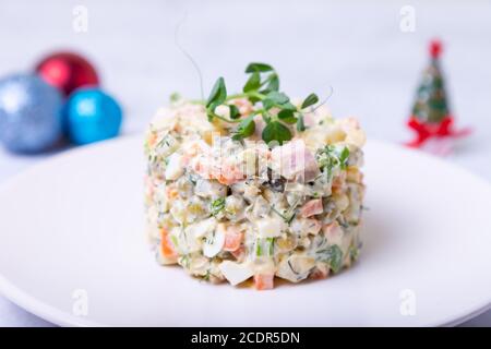 Olivier salad on a white plate, decorated with pea sprouts. Traditional New Year and Christmas Russian salad. Close-up, selective focus, white backgro Stock Photo