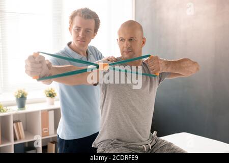 Bald middle aged man stretching resistance band during exercise for arms Stock Photo