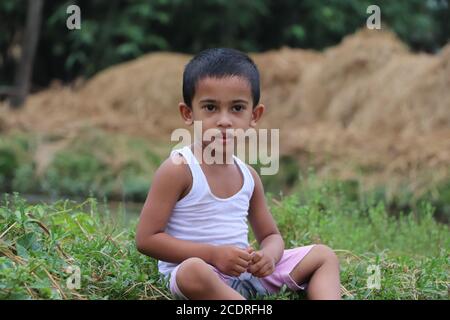 Three years old thoughtful Asian child sitting beside a lake and looking at the camera Stock Photo