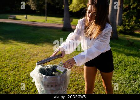 Beautiful well-mannered young woman sets a good example by throwing a waste into the garbage can in the park - Respect the nature concept - Be kind to Stock Photo