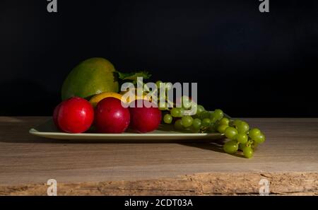 still life with a green bowl on a reflective background with mango,lemons,grapes and plums Stock Photo