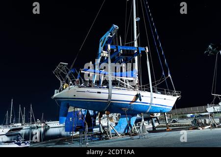 Cagliari, Sardinia, Italy - August 28 2020: boat lift out of the water by an heavy crane machine in the city pier side view at night Stock Photo