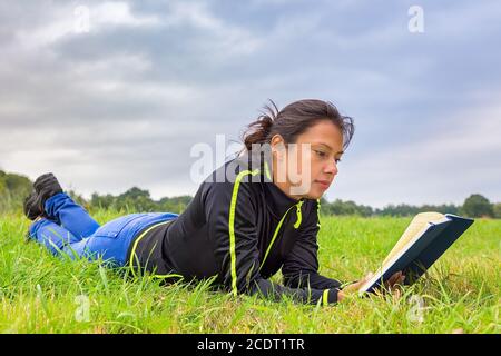 Young woman lying in grass reading book Stock Photo