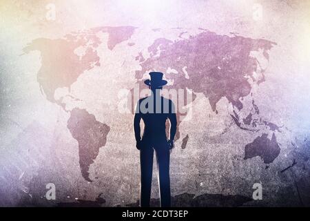Silhouette of a man in hat standing in front of world map on grunge concrete wall Stock Photo