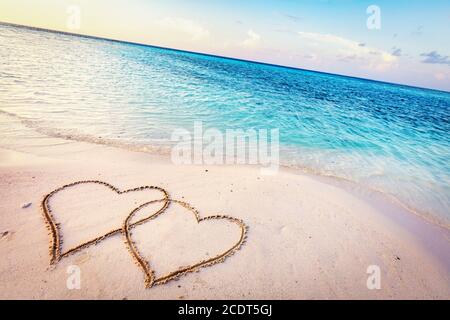 Two hearts drawn on sand of a tropical beach at sunset. Stock Photo