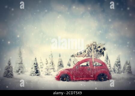 Retro toy car carrying tiny Christmas tree. Fairytale scenery with snow and forest. Stock Photo