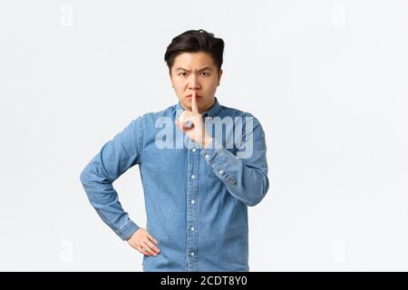 Angry asian man, teacher shushing at disobedient student, looking displeased. Man scolding person being too loud, shushing, say shh with finger Stock Photo