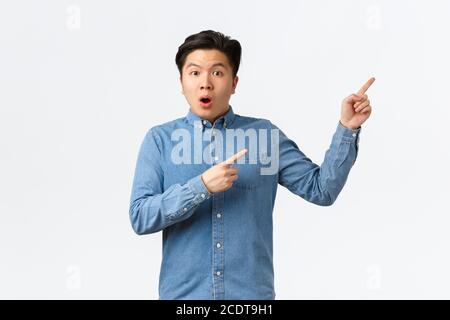 Shocked and astonished asian man asking question about product or announcement. Guy looking startled, pointing fingers upper right corner curious Stock Photo