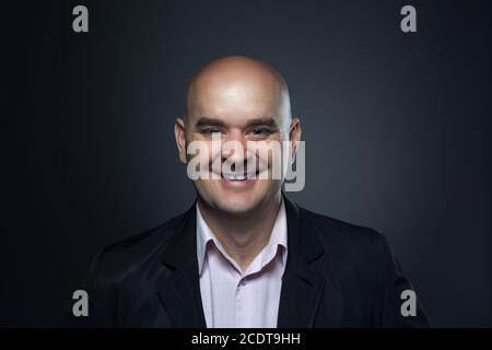 Portrait of a bald smiling, affable man in a suit against a dark background Stock Photo