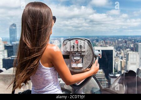 New York City tourist travel woman looking at view of skyline with binoculars from skyscraper rooftop building. Girl traveling in USA summer holidays Stock Photo